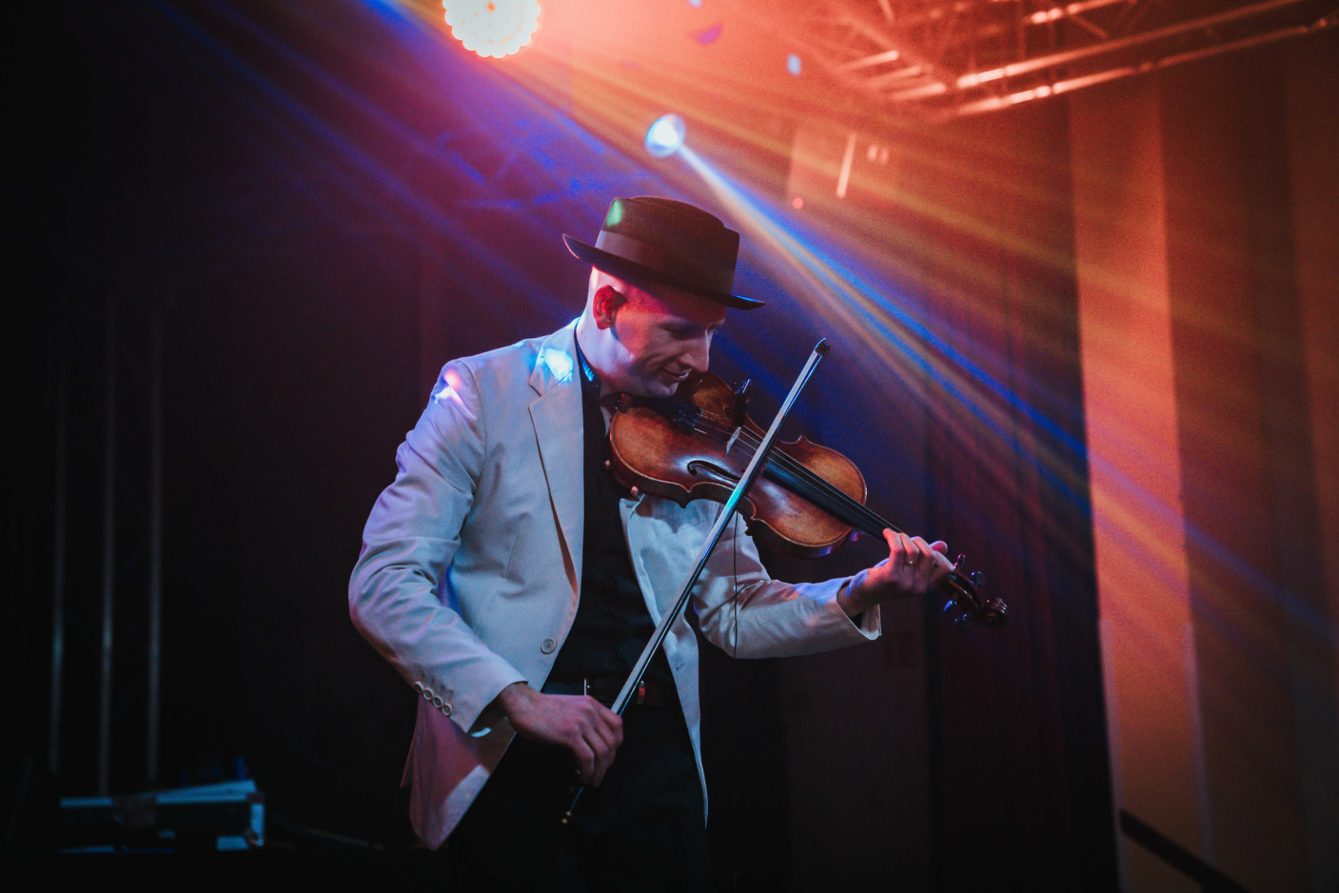 Detail Mr. Violingtona v klobouku a krémovém saku v červeném a modrém jevištním světle